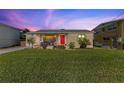 Tan brick home with red door, and a spacious lawn at dusk at 505 Wisteria Rd, Daytona Beach, FL 32118