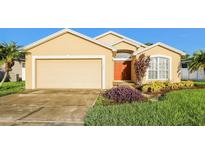 Tan house with a two-car garage, landscaping, and a red door at 8021 Princeton Manor Cir, Lakeland, FL 33809