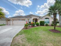 One-story house with beige exterior, two-car garage, and lush landscaping at 1751 Ashwood Run, The Villages, FL 32162