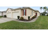 Tan two-car garage villa with red shutters, landscaping, and green lawn at 27231 White Plains Way, Leesburg, FL 34748