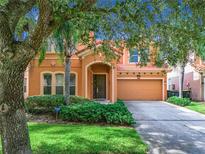 Two-story house with orange exterior, two-car garage, and lush landscaping at 426 Orange Cosmos Blvd, Davenport, FL 33837