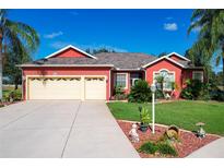 Attractive red house with three-car garage and landscaped yard at 25611 Maurepas Ln, Leesburg, FL 34748