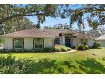 One-story home with brown roof, white walls, and teal front door; landscaped yard with lush green grass at 12810 Anderson Hl, Clermont, FL 34711