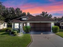 One-story house with brown roof and screened garage door, nestled in a landscaped yard at 22204 Caledonia Dr, Leesburg, FL 34748