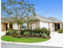 Tan two-car garage villa with a landscaped yard and walkway at 928 Nuthatch Ave, The Villages, FL 32163