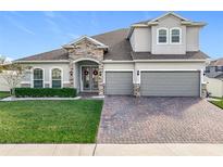 Two-story house with stone accents, three-car garage, and manicured lawn at 405 Amola Way, Howey In The Hills, FL 34737