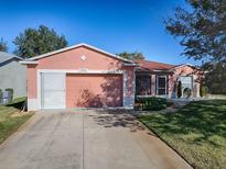 Cute ranch home with a pink exterior, red tile roof, and a two-car garage at 33236 Grand Cypress Way, Leesburg, FL 34748