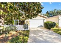 Cute yellow house with white picket fence, attached garage, and nicely landscaped yard at 2102 Estevez Dr, The Villages, FL 32159