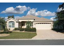 Tan one-story house with a two-car garage and landscaped front yard at 1443 Greenville Way, The Villages, FL 32162