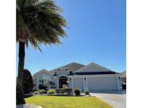 Beautiful single-story home with a gray exterior, lush landscaping, and a three-car garage at 2850 Apache Ct, The Villages, FL 32163