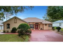 Single-story home with a red door, large driveway, and landscaped yard at 5509 Grove Mnr, Lady Lake, FL 32159