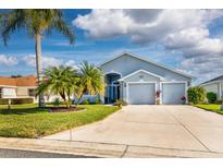 Two-car garage, light gray house with palm trees and manicured lawn at 5717 Illumination Ln, Leesburg, FL 34748
