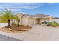 Tan house with palm tree, landscaped yard, and two-car garage at 9224 Se 167Th Ford St, The Villages, FL 32162