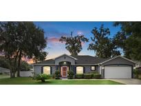 Gray house with red door, two-car garage, and landscaped lawn at 3120 Ne 26Th St, Ocala, FL 34470