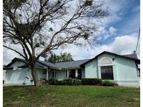 Light teal house with gray roof, landscaping, and a large tree in the front yard at 1470 Ne Old Mill Dr, Deltona, FL 32725