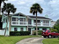 Two-story light teal house with balconies, stone accents, and a landscaped yard at 1012 S Riverside Dr, Edgewater, FL 32132