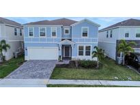 Two-story light blue house with a three-car garage and paver driveway at 3545 Lavender Dr, Davenport, FL 33897