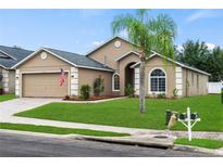 Tan one-story house with two-car garage, palm tree and manicured lawn at 738 Knightsbridge Cir, Davenport, FL 33896