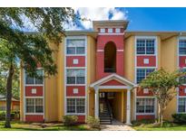 Two-story apartment building with terracotta and yellow exterior, landscaping, and stairs at 3502 Windy Walk Way # 2104, Orlando, FL 32837