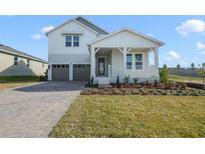 Two-story farmhouse-style home with gray paver driveway and landscaped yard at 488 Toscano St, Clermont, FL 34715