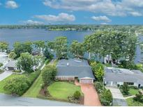 Aerial view of a waterfront home with a private dock, lush landscaping, and a brick driveway at 279 Rippling Ln, Winter Park, FL 32789