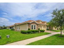 Exterior view of a tan house with a two-car garage and well-manicured lawn at 1068 Quaker Ridge Ln, Champions Gate, FL 33896