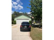 Light green house with a two-car garage and landscaping at 84 Twin Lake Cir, Umatilla, FL 32784