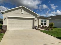 Beige house with a two-car garage and landscaping at 5639 Costa Blanca Way, Davenport, FL 33897