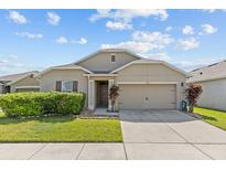 Tan house exterior with two-car garage and landscaping at 5716 Lakeside Landings Blvd, Winter Haven, FL 33881