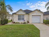 Single-story house with a beige exterior, a white garage door, and a well-manicured lawn at 2977 Kokomo Loop, Haines City, FL 33844