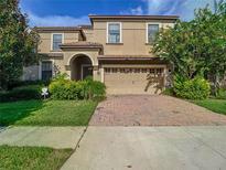 Two-story house with tan exterior, three-car garage, and landscaped yard at 1410 Wexford Way, Davenport, FL 33896