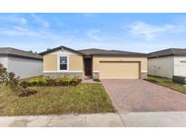 Tan house with dark brown roof, brick driveway and landscaping at 3206 Viceroy Ct, Poinciana, FL 34759