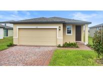 Tan house with a two-car garage, brick driveway, and landscaping at 3551 Broadwing Blvd, Poinciana, FL 34759