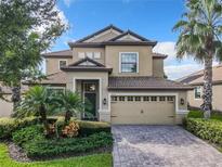 Two-story house with tan exterior, two-car garage, and manicured landscaping at 8920 Dove Valley Way, Davenport, FL 33896
