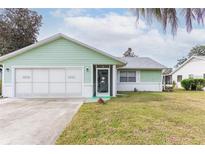 Light green house exterior with a two-car garage and well-maintained lawn at 16 Easter Ross Ct, Leesburg, FL 34788