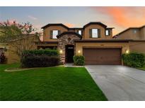 Two-story house with a brown garage door and lush green lawn at sunset at 5009 Torchwood Dr, Minneola, FL 34715