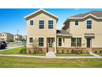 Two story townhome with tan siding, stone accents, and landscaping at 164 Holly Village Dr, Davenport, FL 33837