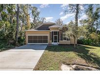 Tan house with stone accents and a screened porch, two car garage, and landscaped yard at 1989 Marsh Hen Vlg, Deland, FL 32720