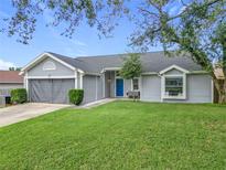 Gray house with a blue door, two-car garage, and well-manicured lawn at 7471 Crooked Lake Cir, Orlando, FL 32818