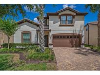 Two-story home with brown accents, a three-car garage, and a brick driveway at 8881 Qin Loop, Kissimmee, FL 34747