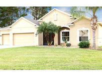 Tan one-story house with three-car garage and manicured lawn at 4420 Heritage Trl, Leesburg, FL 34748