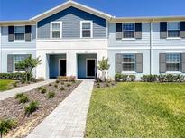 Two-story townhome with light blue and gray siding, a paved walkway, and a well-manicured lawn at 617 Jasmine Ln, Davenport, FL 33897