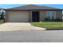 Tan one-story house with a two-car garage and a neatly landscaped lawn at 16344 Blooming Cherry Dr, Groveland, FL 34736
