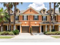 Front view of two story townhouses with attached garages, lush landscaping, and palm trees at 875 Assembly Ct, Reunion, FL 34747