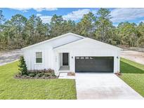 White house with black garage door, landscaping, and a long driveway at 12590 Sw 89Th St, Dunnellon, FL 34432