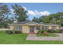 Cute yellow house with a purple door, landscaping, and paved driveway at 610 Litchfield Way, Orlando, FL 32803