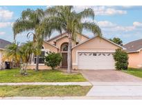 Tan house with palm trees, two-car garage, and brick driveway at 12618 Lynchburg Ct, Orlando, FL 32837