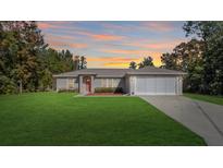 Charming single-story home with a red door, two-car garage, and lush green lawn at sunset at 3891 Sw 130Th Loop, Ocala, FL 34473