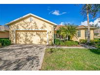 Yellow single-story home with a two-car garage, landscaped yard, and paver driveway at 111 Bell Tower E Xing, Poinciana, FL 34759