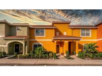 Two-story townhome with orange and green exterior, landscaping, and a walkway at 8931 Bismarck Palm Rd, Kissimmee, FL 34747